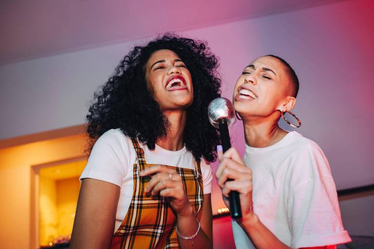 Duas mulheres cantam animadamente segurando um microfone