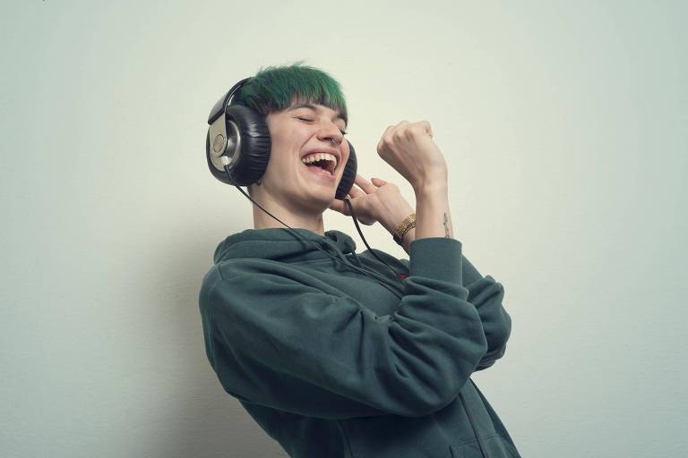 Pessoa canta animadamente usando fones de ouvido e segurando microfone imaginário