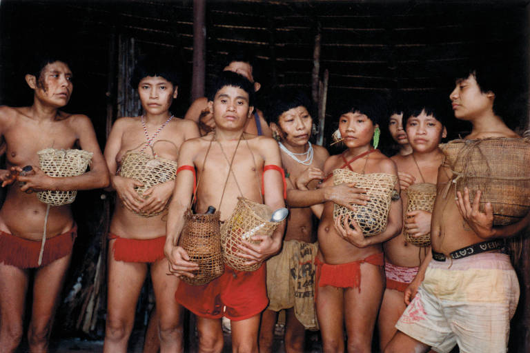 pessoas indígenas usam tangas e bermudas, exibem cabaças decoradas por redes, estão sérias