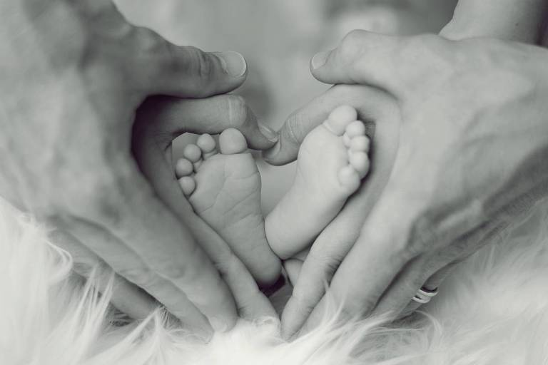 Pai e mãe usam as mãos em volta dos pés de um bebê para fazer um coração