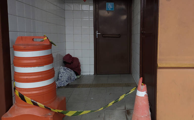 Sem-teto se acomoda na entrada do sanitário da estação Parque Dom Pedro 2º, o principal banheiro público utilizado pela população que vive nas ruas da capital paulista