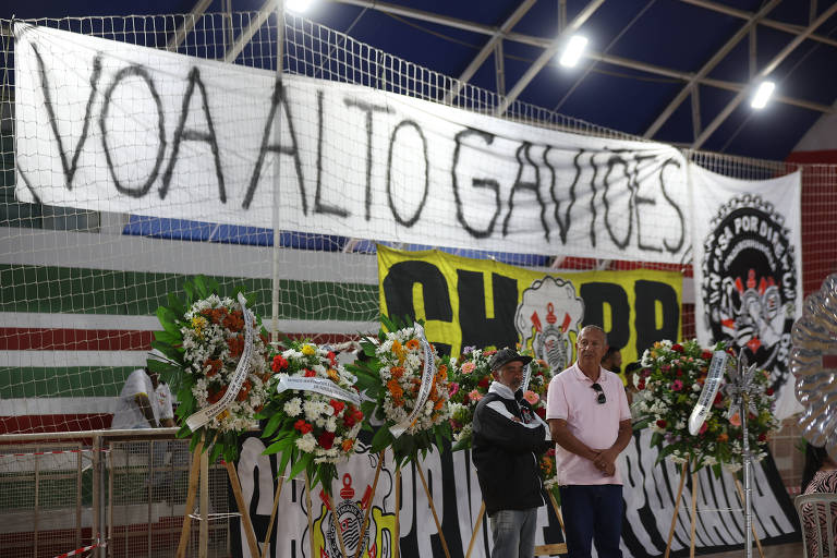 Dois homens entre coroas de flores em homenagem aos torcedores corintianos mortos em acidente de ônibus