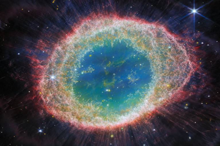 Imagem de nebulosa que lembra um anel (em seu centro) ou um olho humano, pela sua forma achatada ao redor do círculo central; no centro, há a cor azul; ao redor, tons amarelados; a forma final é contornada pela cor vermelha
