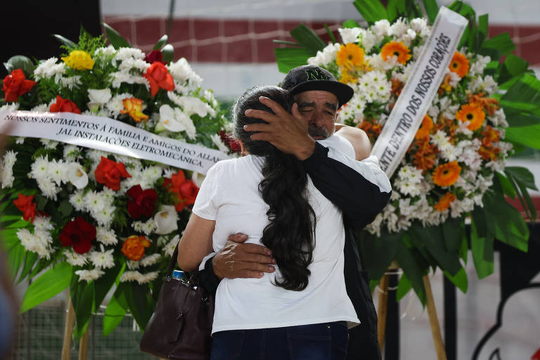 Casal chorando se abraça em frente a duas coroas de flores na homenagem aos torcedores corintianos mortos em acidente de ônibus