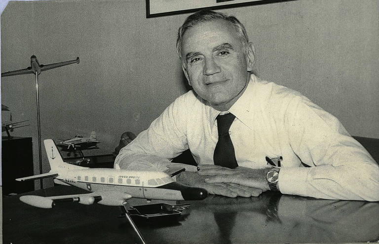 Homem de camisa branca e gravata, em frente a modelos de avião