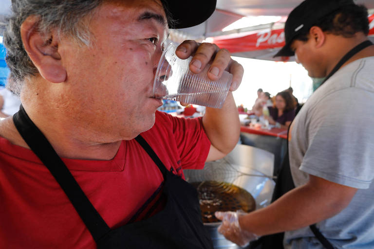 Ao lado da chapa com óleo fervendo, o pasteleiro Mitsuro Omini tenta se refrescar com muita água em feira na Pompeia