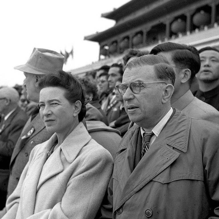 Mulher e homem em meio a outras pessoas durante cerimônia. Prédio da praça em Pequim ao fundo