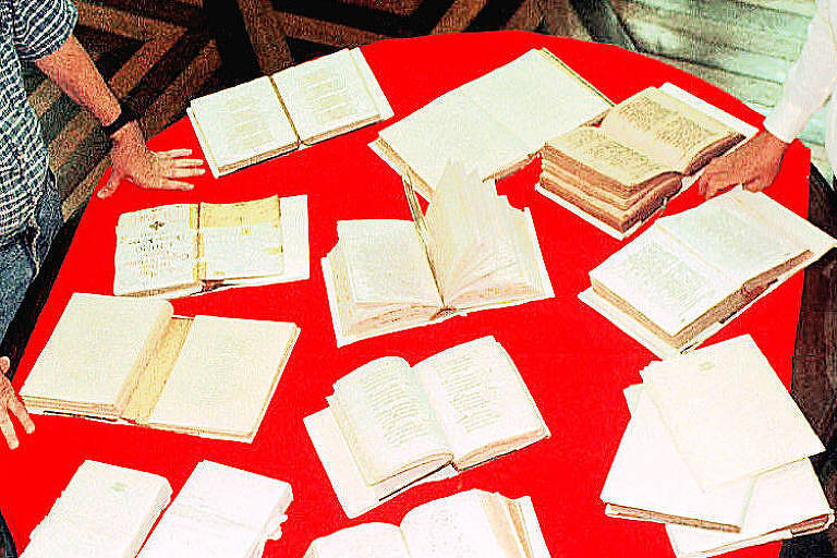 livros antigos dispostos em cima de mesa vermelha