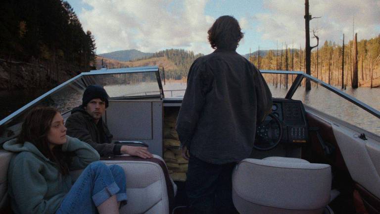Os três atores estão em um pequeno barco. À esquerda, Dakota Fanning e Jesse Eisenberg estão sentados. De pé, guiando o barco, de costas, está Peter Sarsgaard