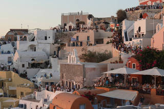 Tourists watch the sunset from the castle of Oia, on the island of Santorini
