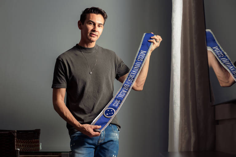 Francisco Aguero, o Mago das Faixas, segura a faixa da Miss Universo Brasil 2023, azul com escritos em prateado