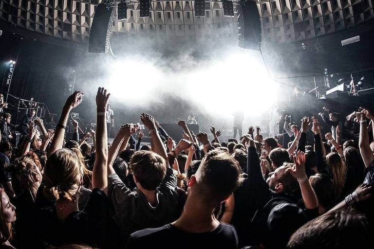 Show musical com muitas pessoas com os braços levantados em frente ao palco iluminado