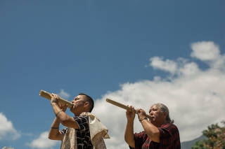 Cody Pueo Pata and Lori Lei Ishikawa blow into pu ?ohe, or hollowed-out bamboo pipes, during a traditional Hawaiian ceremony called a hula, on the island of Maui, Aug. 22, 2023. (Daeja Fallas/The New York Times)