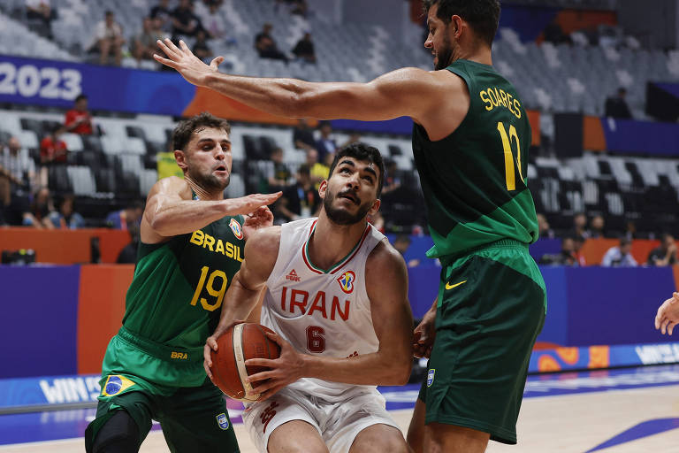 Dois brasileiros, um à esquerda e outro à direita, tentam bloquear os movimentos de um iraniano, ao centro, que tem a bola em mãos