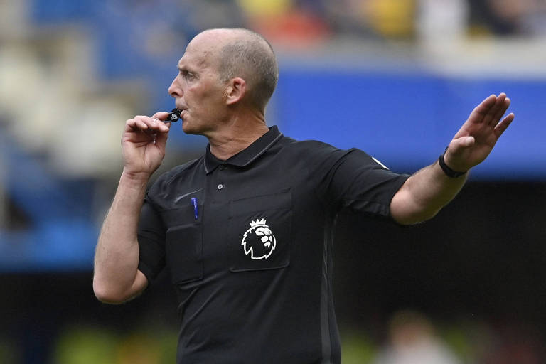 Com uniforme preto, o árbitro Mike Dean, hoje aposentado, sopra seu apito em partida do Campeonato Inglês da temporada 2021/2022