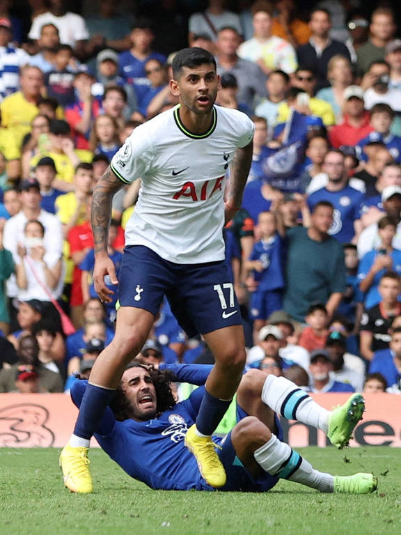 Marc Cucurella, do Chelsea, reclama sentado no gramado depois de ter a cabeleira puxada por Cristian Romero, do Tottenham, que está de pé na frente dele, em partida da Premier League