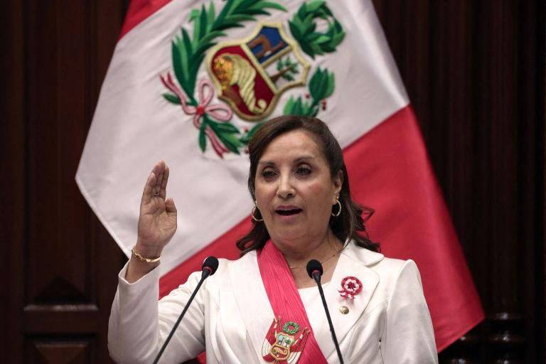 Dina Boluarte, presidente do Peru, discursando em frente a bandeira
