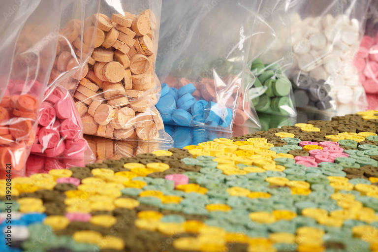 Sacos plásticos e mesa com pílulas coloridas de MDMA apreendidas em operação policial