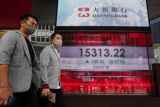 FILE PHOTO: People walk past a screen displaying the Hang Seng stock index at Central district, in Hong Kong