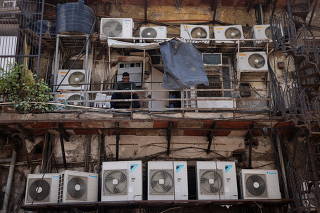 A man uses his mobile phone as he sits amidst the outer units of air conditioners, at the rear of a commercial building in New Delhi