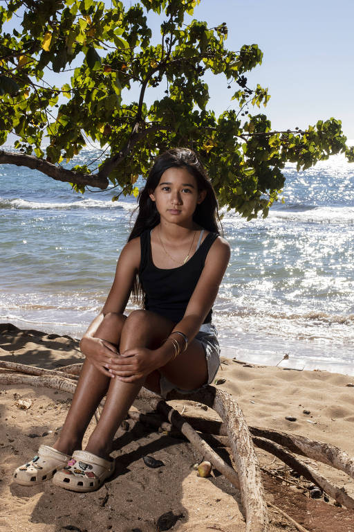 Retrato de jovem sentada na beira de uma praia com o mar ao fundo