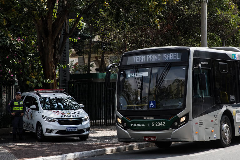 Ônibus com os dizeres "terminal Princesa Isabel" passa pela avenida. Ao lado, em cima da calçada, uma viatura da polícia está estacionada
