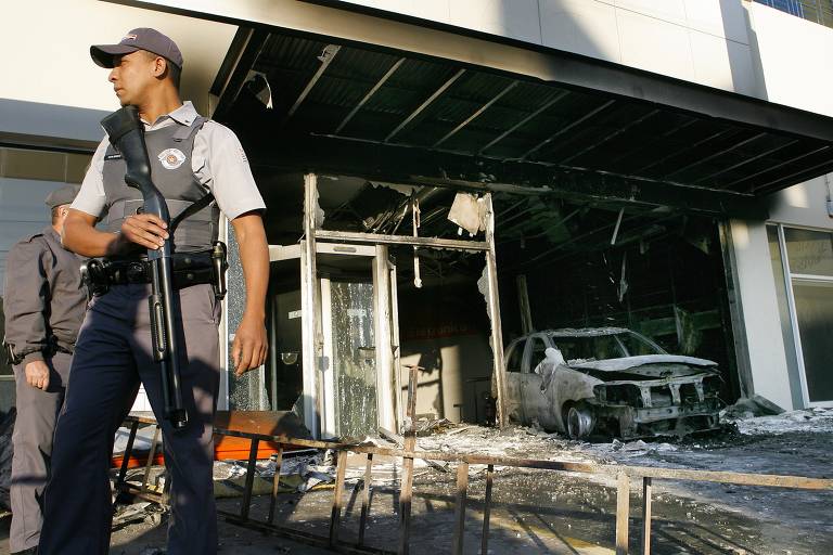 Policiais militares em frente a uma agência bancária do Itaú incendiada por integrantes do PCC na zona sul da capital paulista, durante o grande ataque de 2006