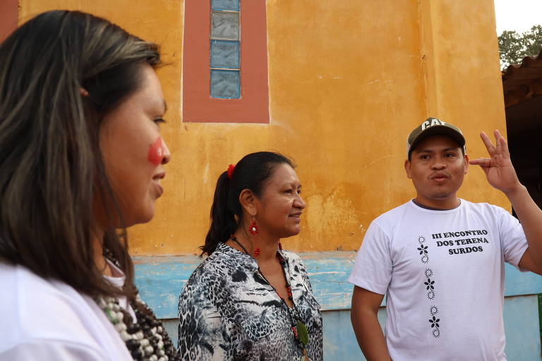 duas mulheres e um jovem indígena; ele usa camisa com dizeres: terceiro encontro dos terena surdos