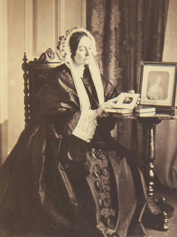 foto de amélia, sentada ao lado de um retrato, por sua vez sobre a mesa