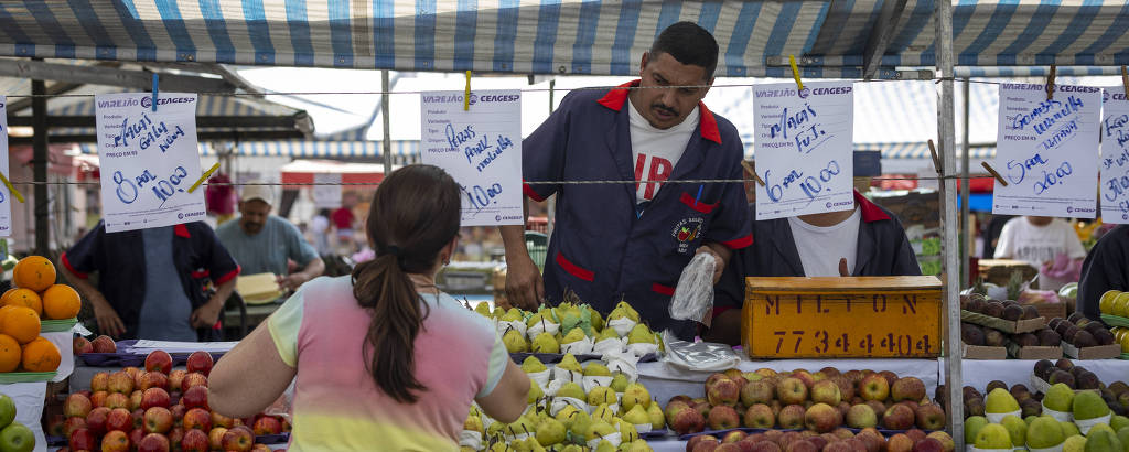 Imagem mostra mulher comprando frutas em uma banca de uma feira