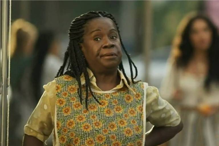 Em foto colorida, mulher negra grava cena de uma novela na praça da cidade cenográfica