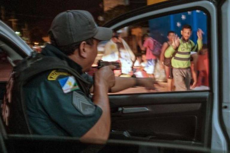 Policial abrindo porta de viatura com a câmera apontada, enquanto homem ao lado ergue as mãos para demonstrar que está desarmado