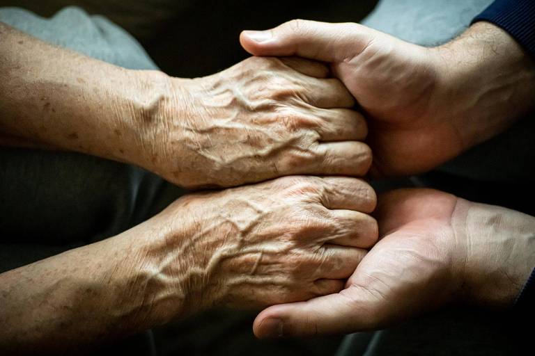 Mãos de pessoa mais velha sendo segurada por mãos mais jovens

