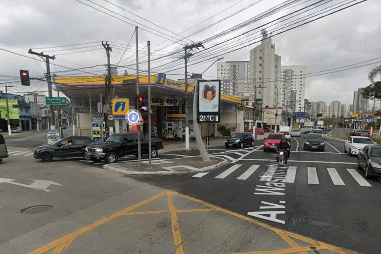 fotografia mostra avenida com bastante tráfego e posto de combustíveis em uma esquina