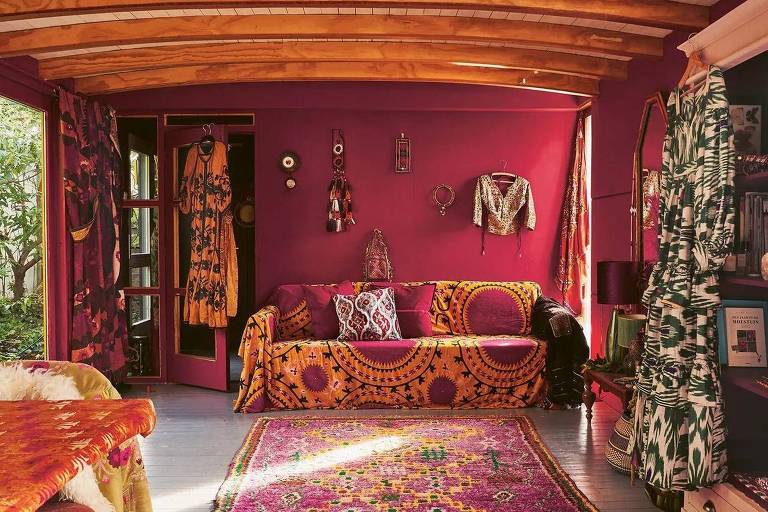 Fotografia colorida mostra uma sala com paredes rosa e roupas penduradas nas paredes e portas
