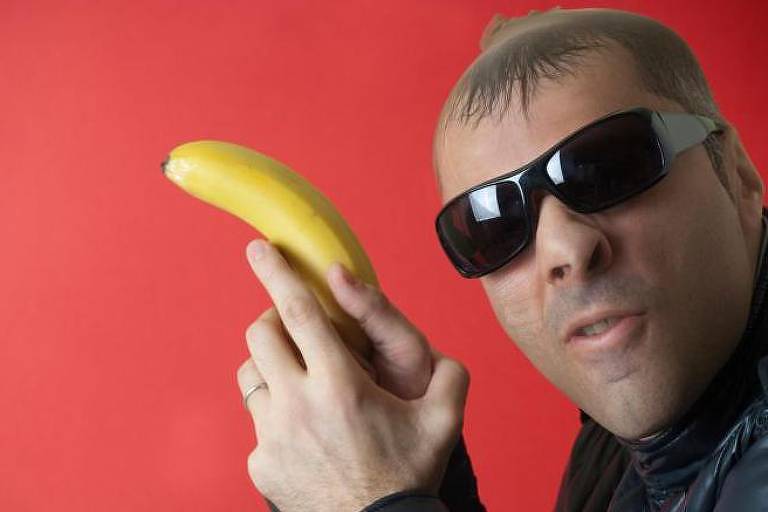 Homem usando óculos escuros empunha uma banana como se fosse uma arma