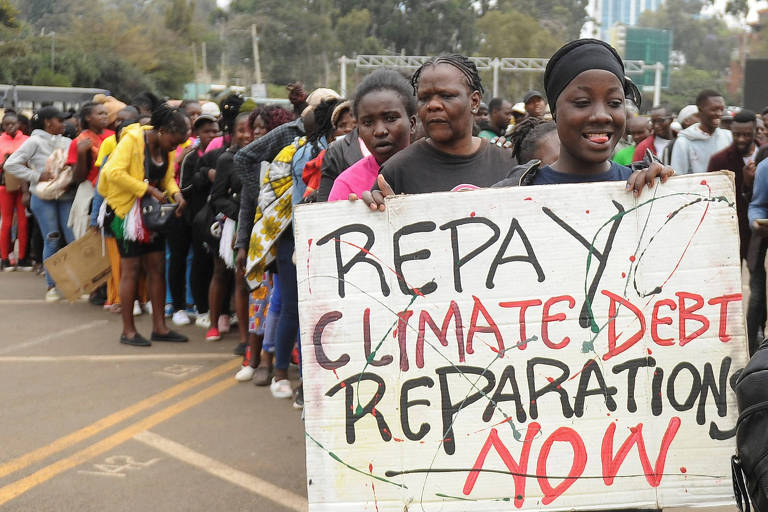 Em fila, mulheres seguram cartaz que diz "repay climate debt reparations now"