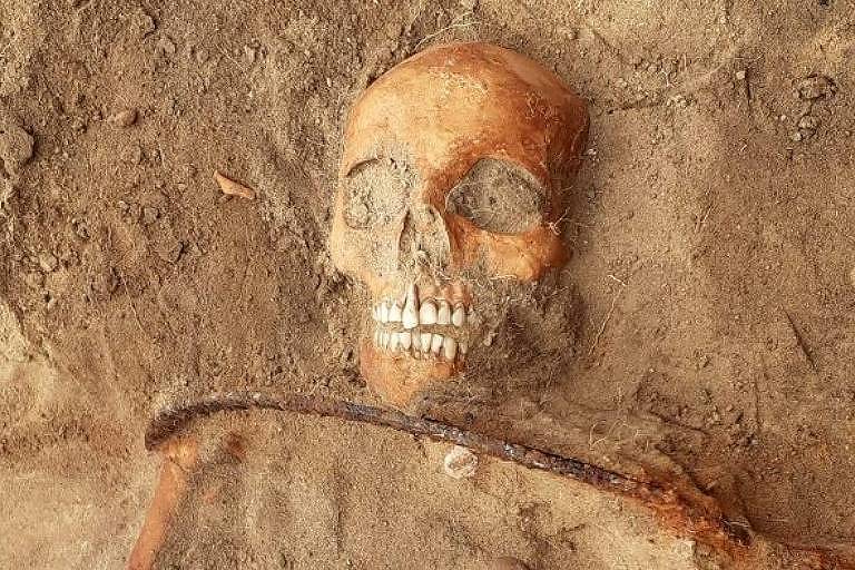 Pesquisadores na Polônia escavaram uma mulher do século 17 enterrada com uma foice no pescoço e cadeado no pé; nas proximidades estavam os restos mortais de uma criança com um cadeado sob o pé