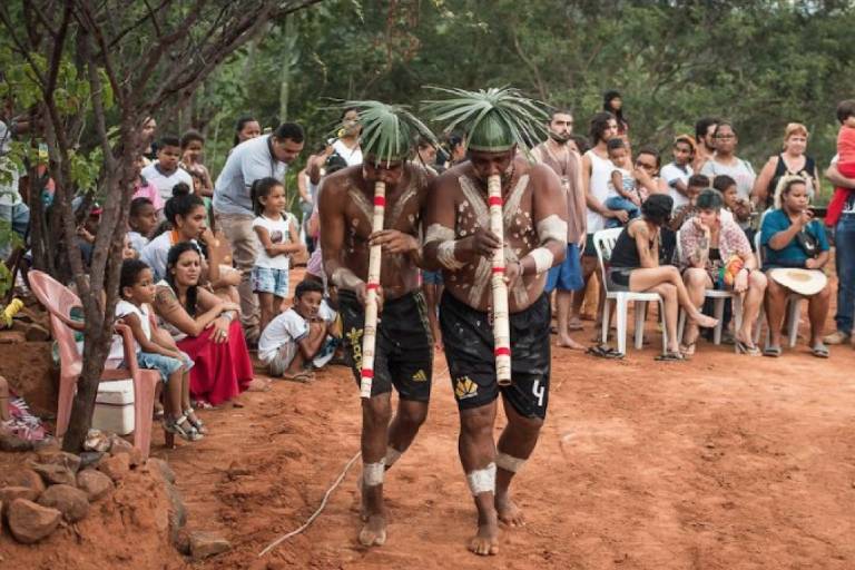 Em foto colorida, dois integrantes do povo pankararu realizam o toré, ritual que reúne dança, música, luta, religião e brincadeiras, tocando flautas