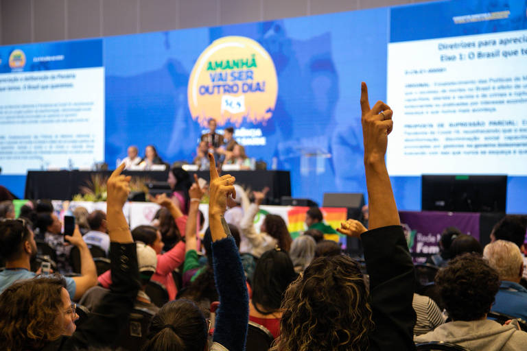 Três pessoas da platéia levantam o dedo indicador durante votação da plenária final da 17ª Conferência Nacional de Saúde.