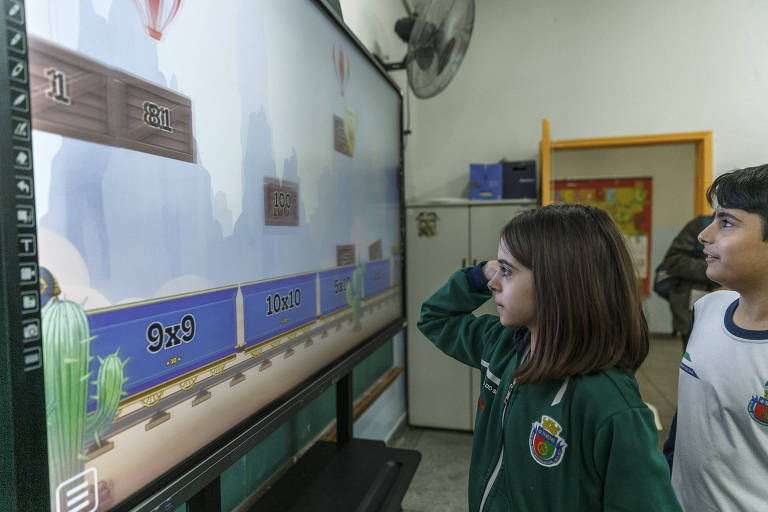 Alunos tocam em lousa digital (touchscreen) para brincar resolvendo exercícios de matemática durante a aula