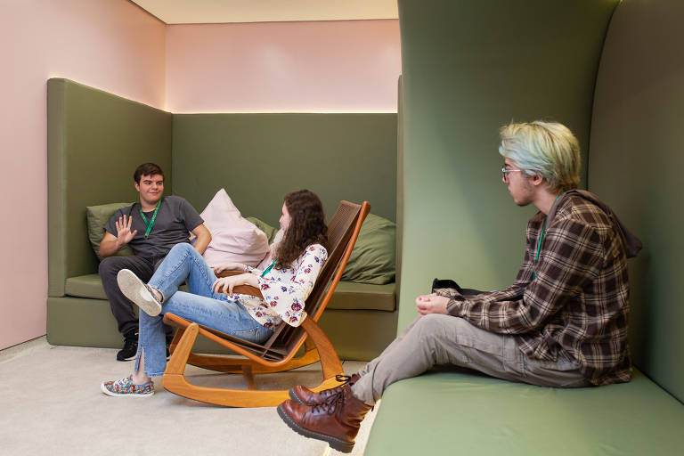 dois meninos e uma menina estão sentados em poltronas e bancos em tom verde, em sala com paredes rosas
