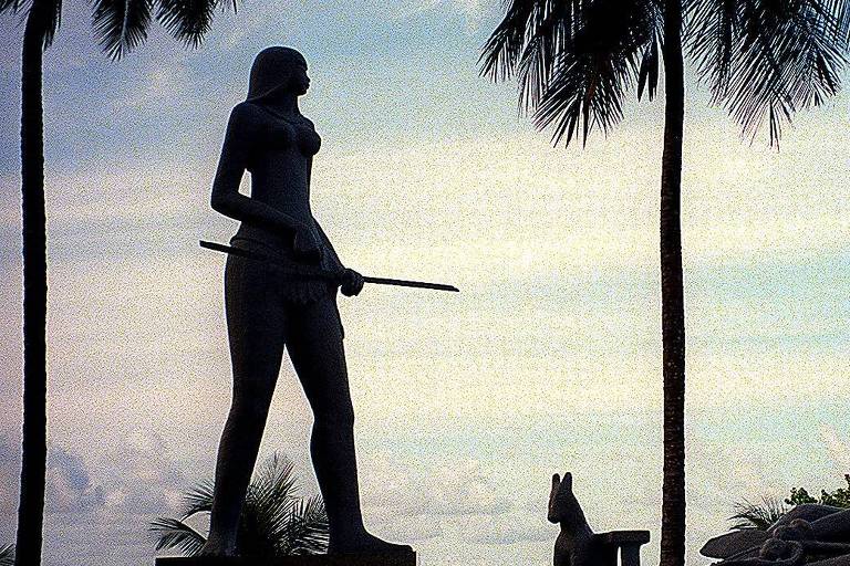 estátua de mulher indígena sob coqueiros contra o pôr do sol