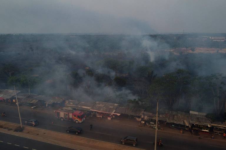 Foto aérea de fumaça densa ao lado de rodovia com caminhões passando