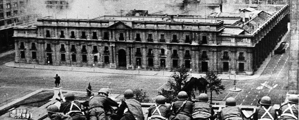 Foto em preto e branco mostra soldados deitados em telhado mirando suas armas ao palácio do governo, que está tomado por fumaça