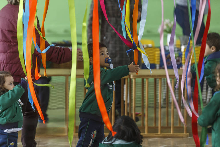 Crianças com chupeta brincam com fitas coloridas presas ao teto em escola