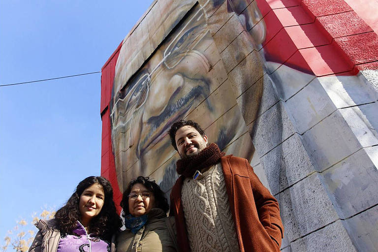 Cecilia Bottai ao lado dos filhos perto do mural pintado em homenagem a seu marido, Patricio Bustos, em 2019, no bairro Yungay, em Santiago