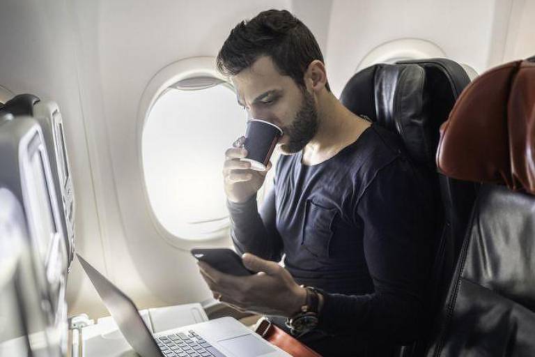 Homem com celular e laptop em avião
