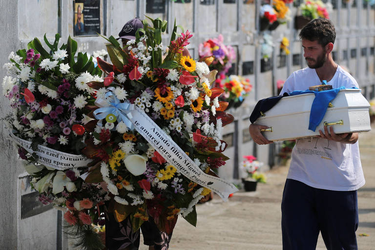 Homem carrega caixão perto de coroa de flores enfeitada com uma faixa que diz: "Amado filho Miguel, te amarei para sempre. Papai"