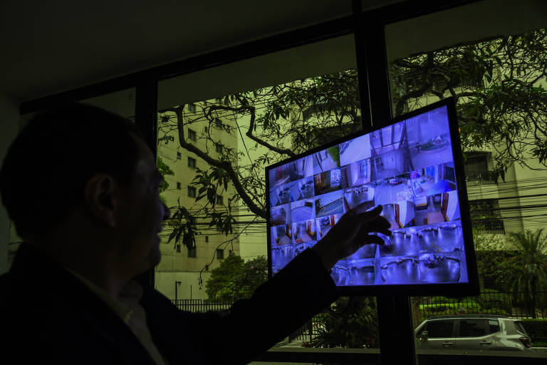 silhueta de homem aponta para imagem em tela de computador que exibe mosaico com imagens de diferentes câmeras 